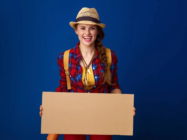 青い背景に空のボードを示す格子縞のシャツで幸せな健康な女性ハイカー — ストック写真