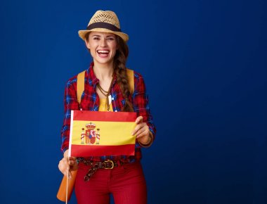 gülümseyen turist kadın İspanya bayrağı mavi arka plan karşı gösterilen sırt çantası ile uygun