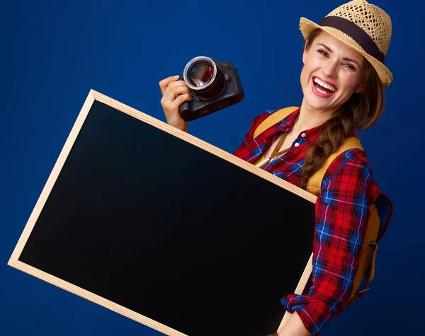 青い背景に空のボードを表示するデジタル一眼レフ カメラに格子縞のシャツの観光女性に合う笑顔 — ストック写真