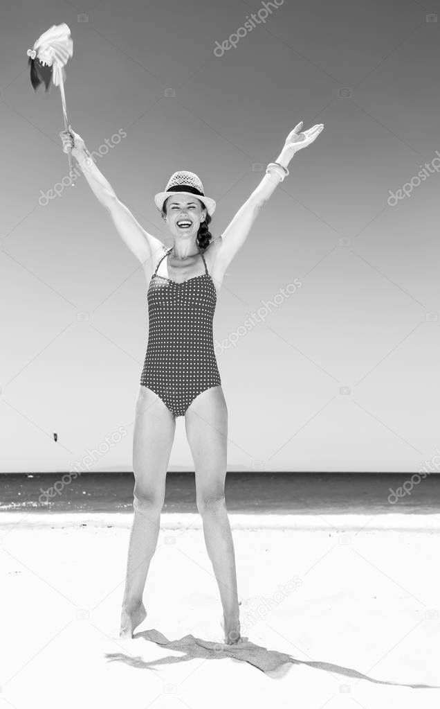 Full length portrait of happy modern woman in bright swimsuit on the seashore with windmill toy rejoicing