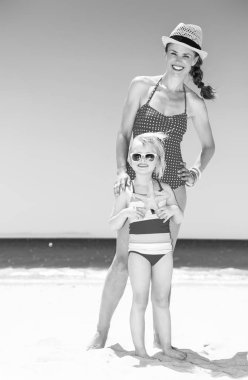 Mutlu genç anne ve kızı sahilde deniz yıldızı tutan parlak beachwear içinde tam uzunlukta portresi