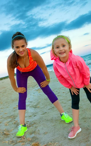 夜のストレッチのビーチでスポーツ スタイルの服で満足してアクティブな母と娘 — ストック写真