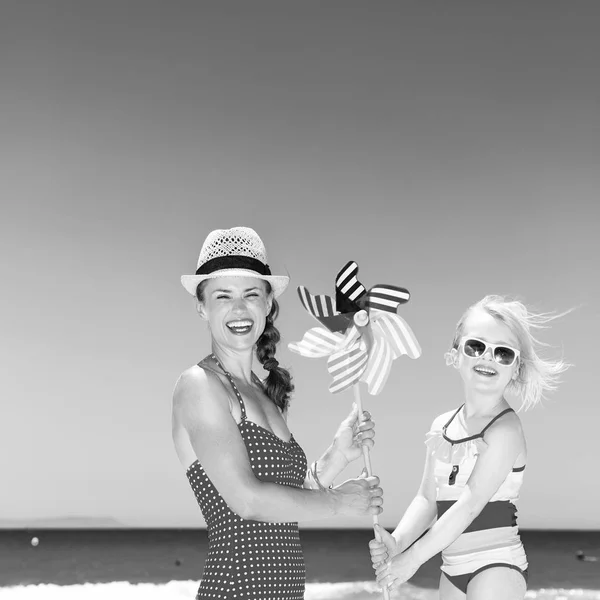 風車のおもちゃをつないでビーチを明るいビーチウェアでモダンな母と娘の笑顔 — ストック写真