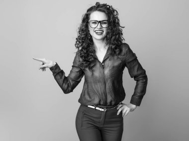 Uzun dalgalı esmer saçlı gözlüklü bir şey gösteren gülümseyen şık kadın