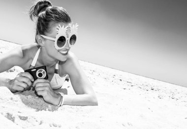 Beyaz kum eğlenceye. gülümseyen güneş gözlüğü ve mayo kopya alanı digital fotoğraf makinesi ile arayan sahil üzerinde modern kadın
