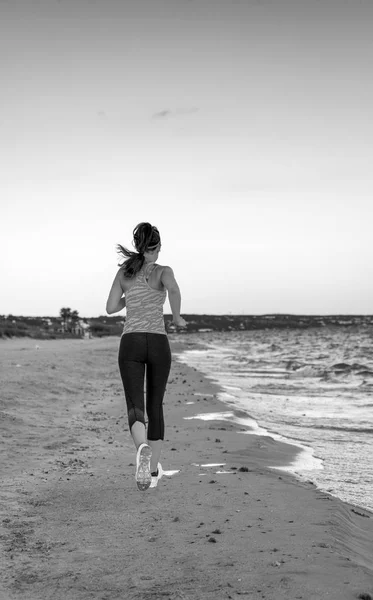 从后面看到健康的妇女慢跑在运动风格的衣服在海边的晚上运行 — 图库照片
