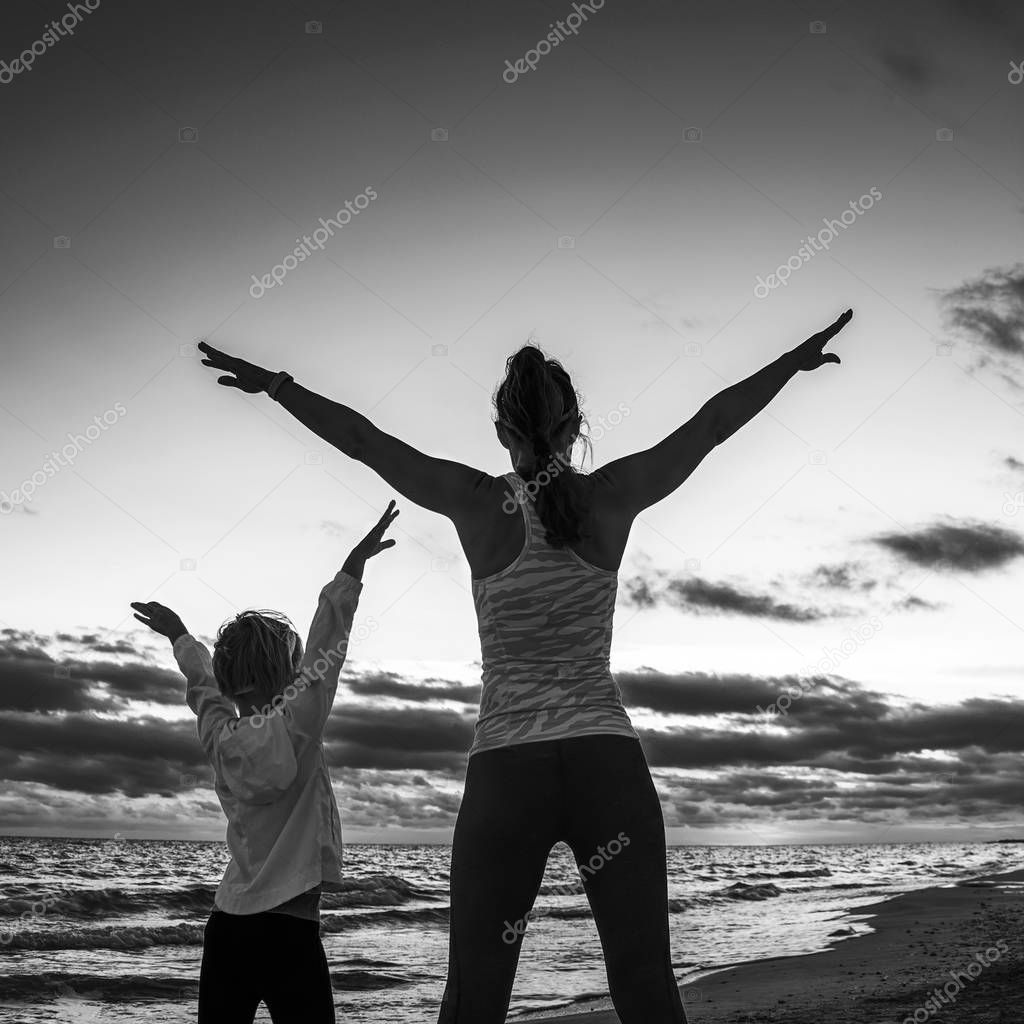active mother and child in sport style clothes on the seashore on the sunset rejoicing