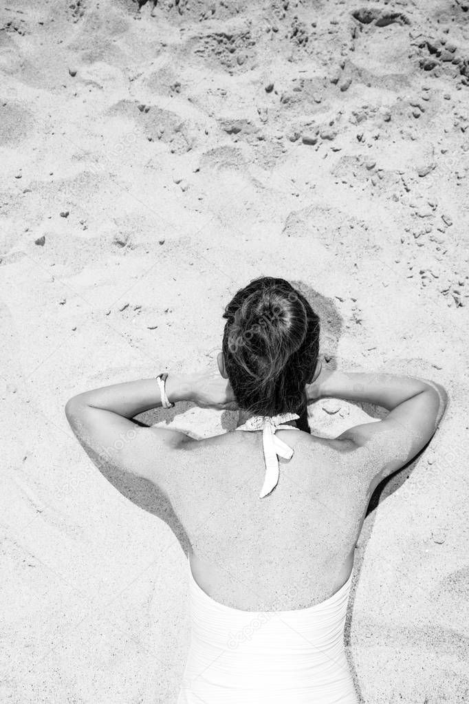 Fun on white sand. Seen from behind modern woman in swimwear laying on the seacoast