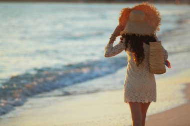 Gün batımında deniz kenarında yürüyen zarif orta yaşlı kadın.