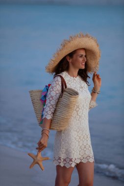Kumsal saman çantası ve deniz yıldızıyla mutlu modern kadın.