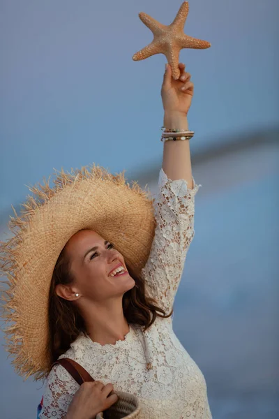 Uśmiechnięta nowoczesna kobieta na plaży o zachodzie słońca trzymająca rozgwiazdy — Zdjęcie stockowe