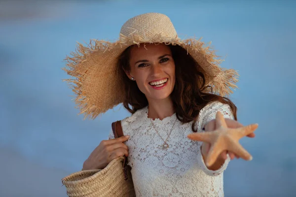 Mujer elegante feliz en la costa del océano al atardecer mostrando estrellas de mar —  Fotos de Stock