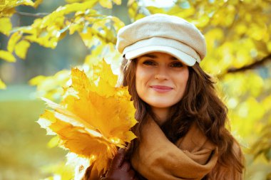 Sarı yapraklı kadın sonbahar parkında yeşilliklerin arasında.