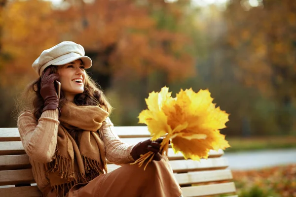 Усміхнена молода жінка з жовтим листям розмовляє на мобільному телефоні — стокове фото