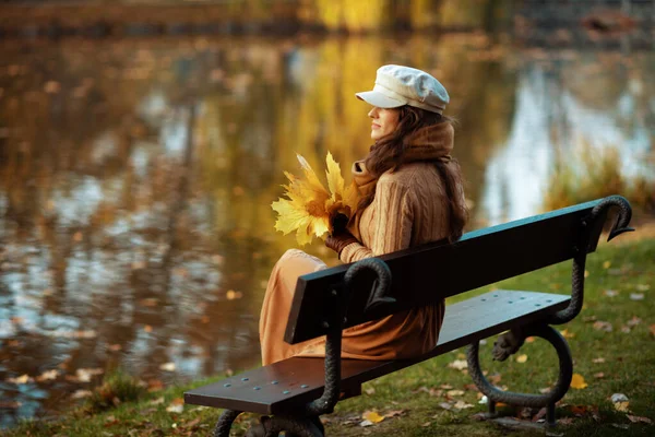 Nachdenkliche stilvolle Frau mit gelben Blättern, die in die Ferne blickt — Stockfoto