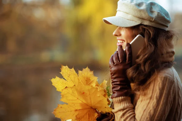 Glückliche stilvolle Frau mit gelben Blättern per Handy — Stockfoto