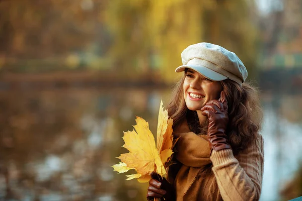 노란 나뭇잎을 가진 웃는 여자가 전화로 얘기하는 모습 — 스톡 사진