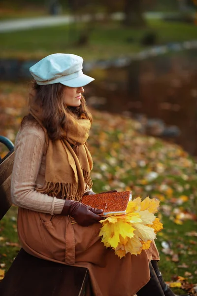 pensive modern middle age woman with notebook and yellow leaves