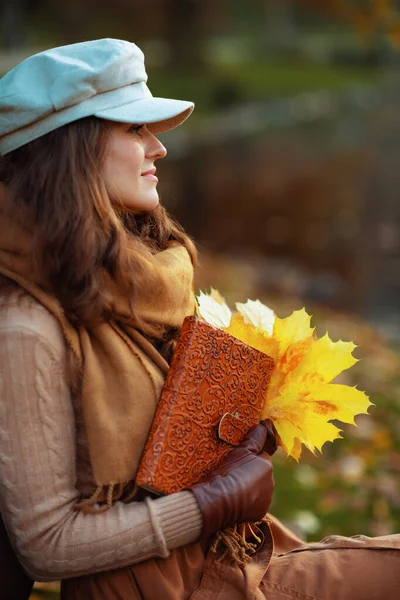 Pensive middle age woman with notebook and yellow leaves — Stock Photo, Image