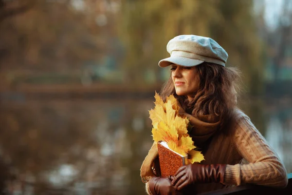 Pensive elegante vrouw met bruine notebook en gele bladeren — Stockfoto