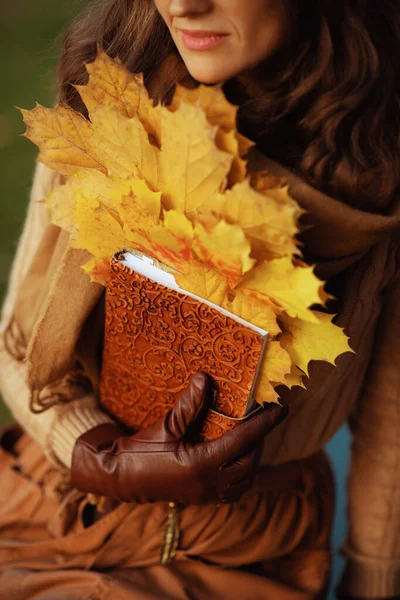 Крупный план задумчивой женщины с коричневым блокнотом и желтыми листьями — стоковое фото