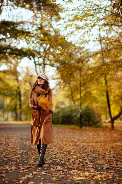 ผู้หญิงมีความสุขที่มีใบสีเหลืองเดินออกไปข้างนอกในสวนฤดูใบไม้ร่วง — ภาพถ่ายสต็อก
