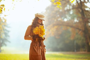 Sonbahar parkında sarı yapraklı, güler yüzlü bir kadın.