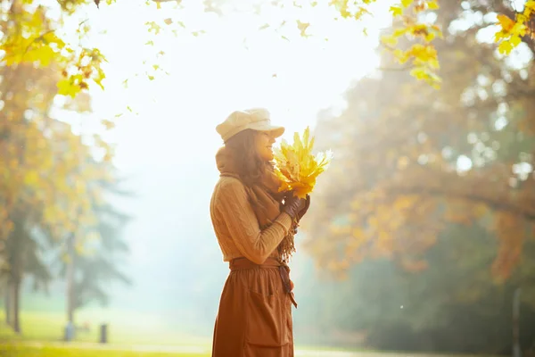 smiling trendy woman with yellow leaves outdoors in autumn park