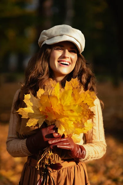 Donna sorridente fuori nel parco di autunno che tiene i fogli gialli — Foto Stock