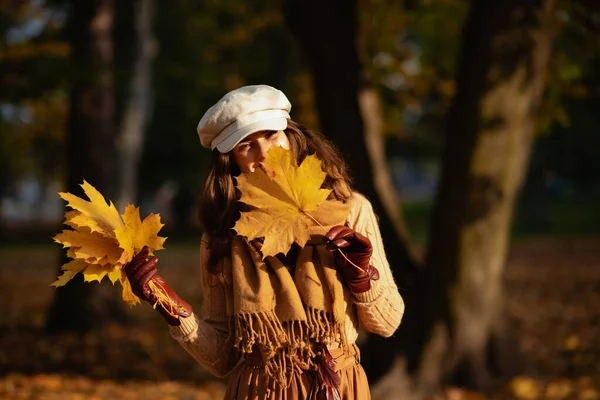 Young woman outdoors in autumn park hiding behind yellow leaf — Stock Photo, Image