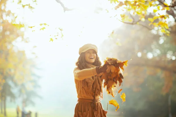 Frau wirft im Herbstpark Stapel gelber Blätter nach draußen — Stockfoto