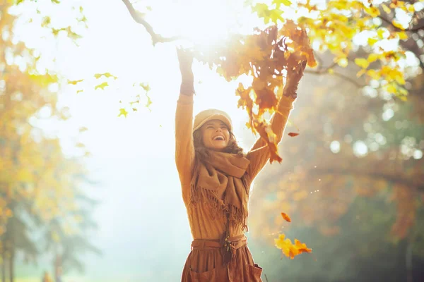 Woman outside in autumn park throwing up pile of yellow leaves — Stock Photo, Image