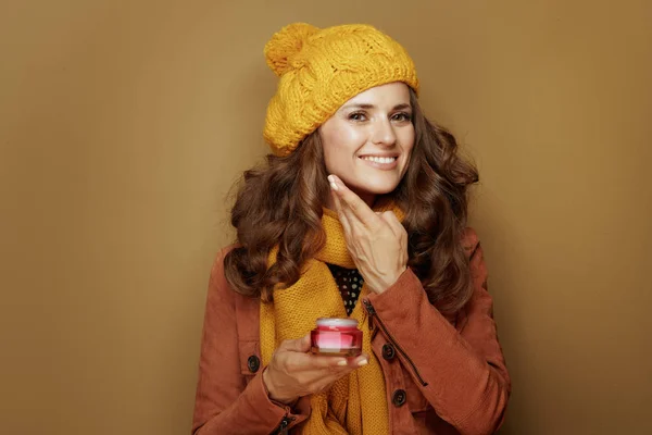 Mujer joven feliz usando crema facial sobre fondo marrón — Foto de Stock