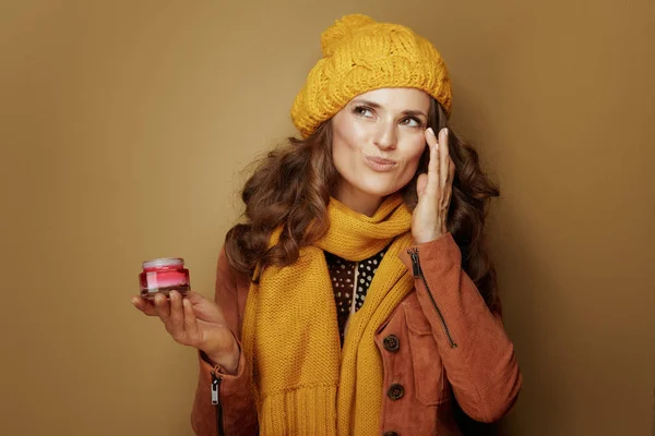 Mujer moderna usando crema facial aislada sobre fondo de bronce — Foto de Stock