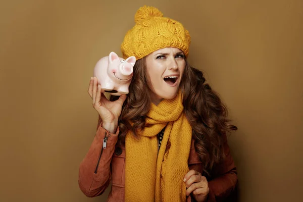 Überraschte Frau schüttelt Sparschwein vor beigem Hintergrund — Stockfoto