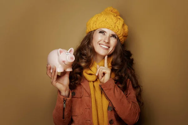 Pensive modern woman with piggy bank isolated on beige — Stock Photo, Image