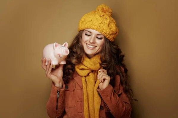 Sorrindo mulher olhando para porquinho banco contra fundo marrom — Fotografia de Stock