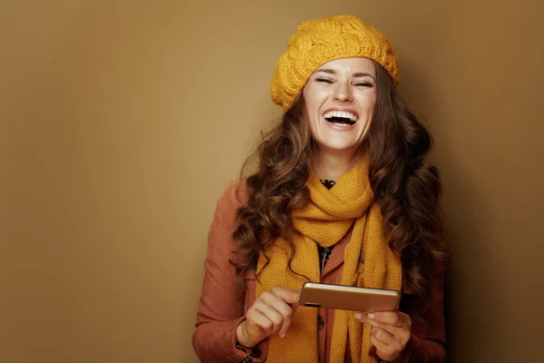 Sorrindo jovem com telefone e mensagens de texto em fundo marrom — Fotografia de Stock