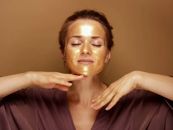 Ontspannen elegante vrouw met gouden masker het maken van gezichtsmassage — Stockfoto