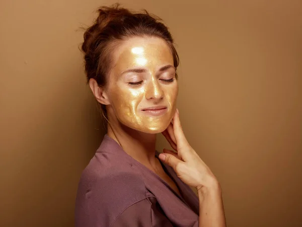 Yüzüne dokunan altın kozmetik maskeli modern kadın — Stok fotoğraf