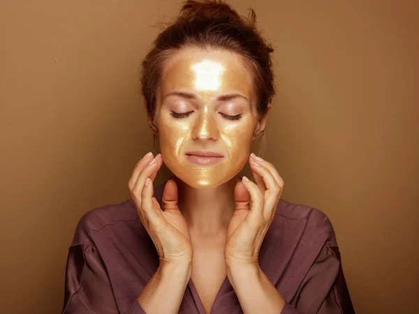 Elegante huisvrouw met gouden masker het maken van gezicht zelf massage — Stockfoto