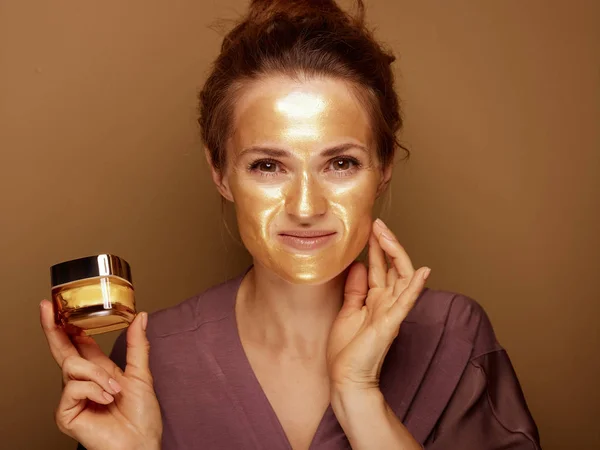 Vrouw met gouden masker houden crème en aanraken gezicht — Stockfoto