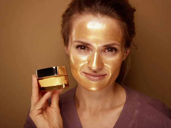 Женщина в золотой маске показывает крем на бронзовом фоне — стоковое фото