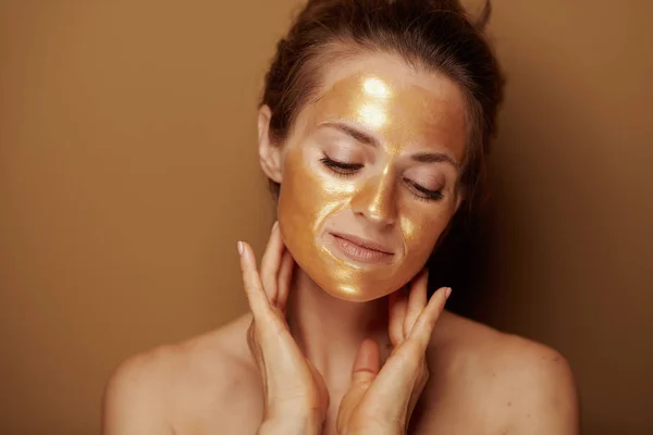 Zrelaksowana kobieta ze złotą maską na beżowym tle — Zdjęcie stockowe