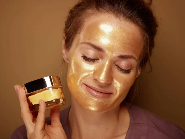 Zrelaksowana kobieta ze złotą maską trzymająca butelkę kremu do twarzy — Zdjęcie stockowe