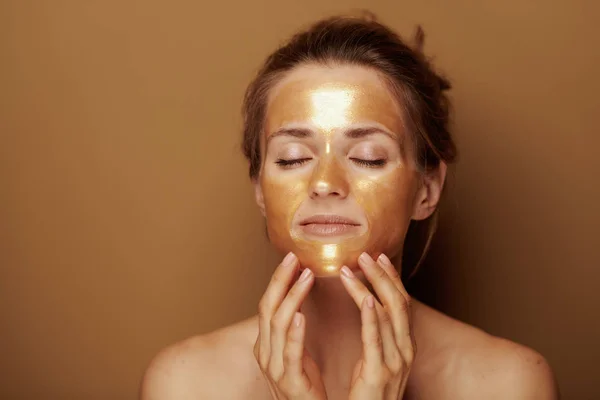 Donna moderna con maschera dorata facendo massaggio facciale auto — Foto Stock
