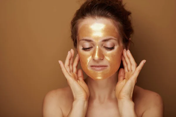 Moderne vrouw met gouden masker het maken van gezicht zelf massage — Stockfoto