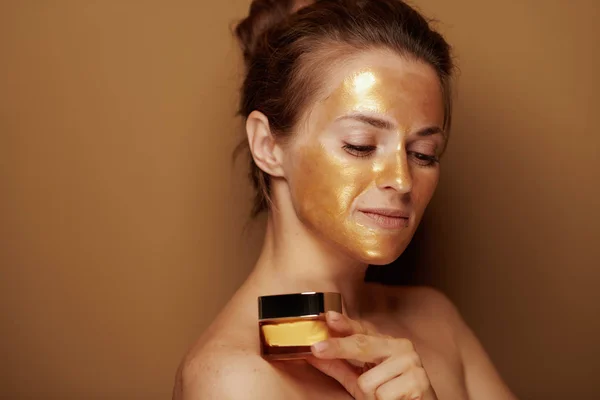 Nowoczesna kobieta ze złotą maską trzymająca butelkę kremu do twarzy — Zdjęcie stockowe