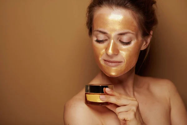 Домохозяйка в золотой маске смотрит на бутылку крема для лица — стоковое фото