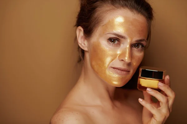 Huisvrouw met gouden masker houden crème op bronzen achtergrond — Stockfoto